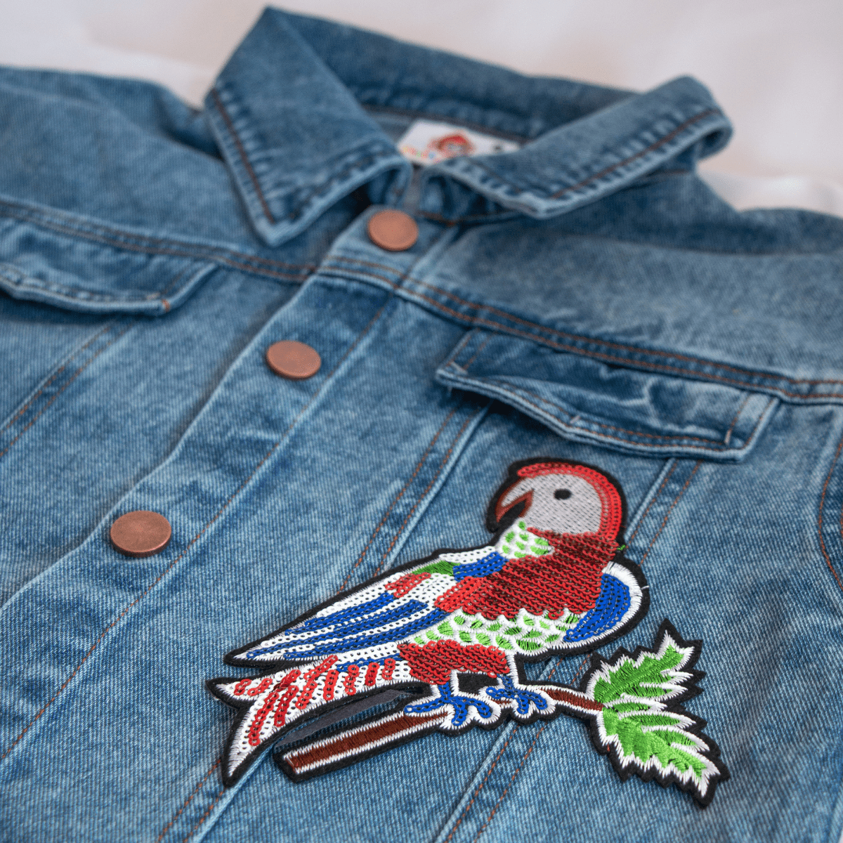 Dunkelblaue Jeansjacke für Kinder mit glitzerndem Papagai-Bügelbild – ein kreatives und funkelndes Statement-Piece.